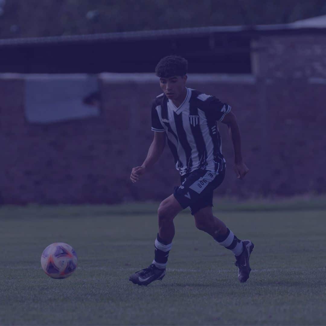 start-the-season-strong-featured (1) A soccer player in a black and white striped uniform runs on a grassy field, focused on a colorful soccer ball in front of him. A brick wall and trees are visible in the background.